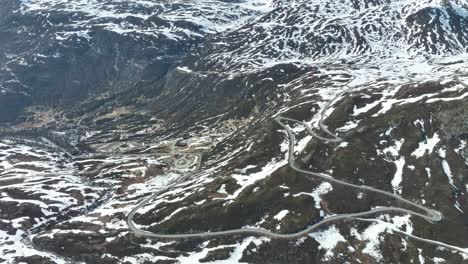 Sognefjellet-mountain-road-descent-towards-Turtagro-and-Skjolden-in-Luster-Sogn-Norway---Springtime-aerial-with-melting-snow-patches-left-in-landscape-and-road-winding-down-hillside