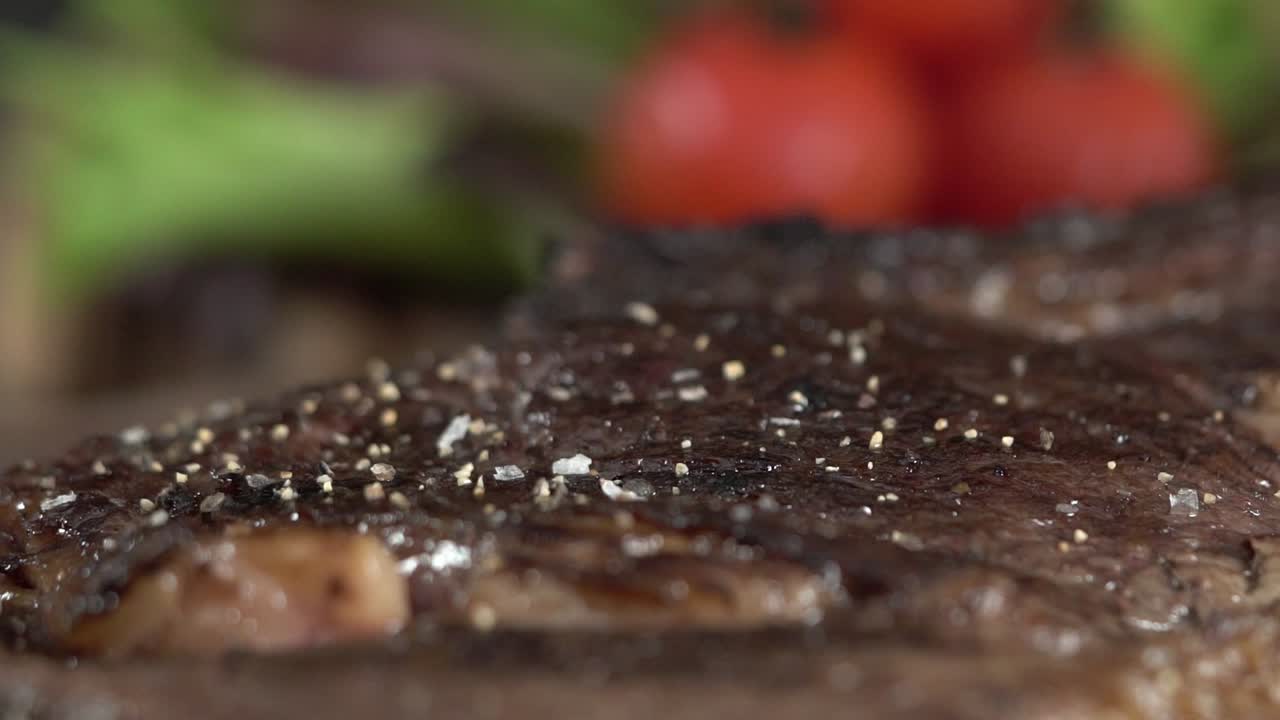 A tasty steak cooked well-done seasoning in extreme close up shot. Adding season salt and black pepper recipe over a grilled piece of meat, slow motion.