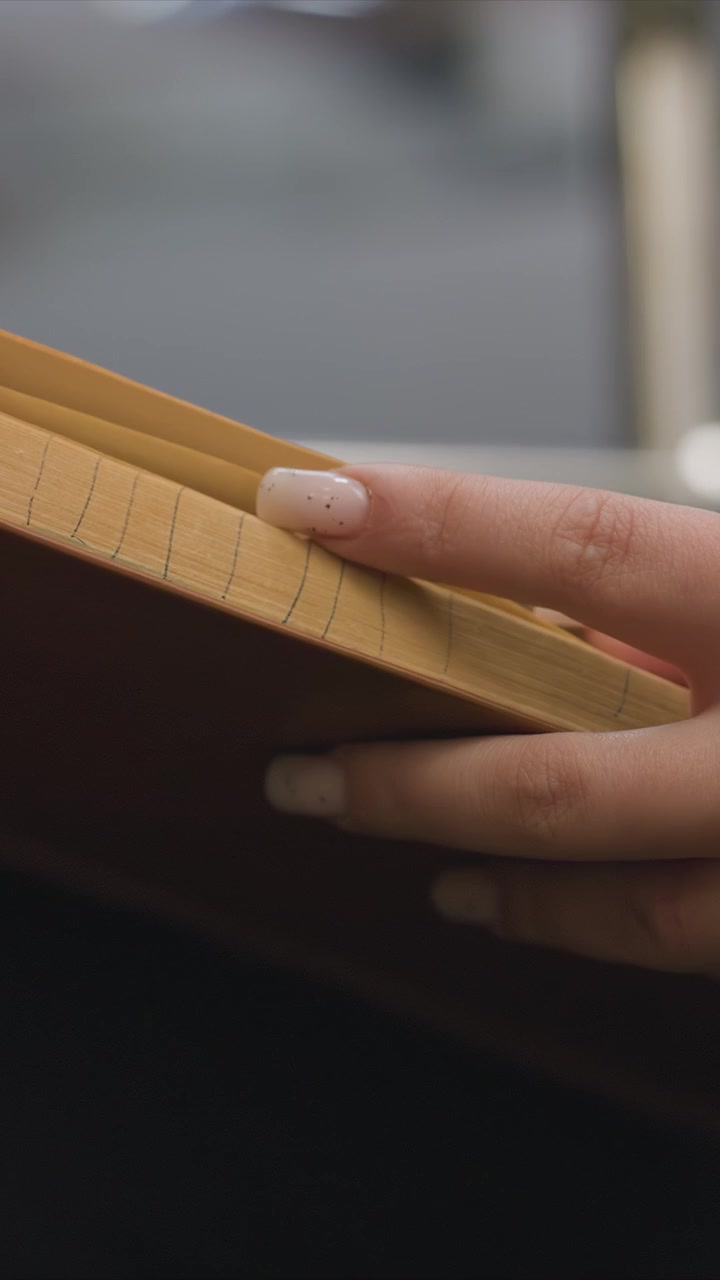 Dita leggere afferrano e aprono un volume ben usato. La texture del legno sul bordo delle pagine spesso sfogliate è chiara. Un delicato gioco di ombre aggiunge profondità alle mani e alle superfici della carta.