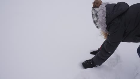 Hands-of-Young-Woman-in-Gloves-and-Warm-Clothes-Taking-Snow-From-Field-on-Cold-Winter-Day,-Slow-Motion