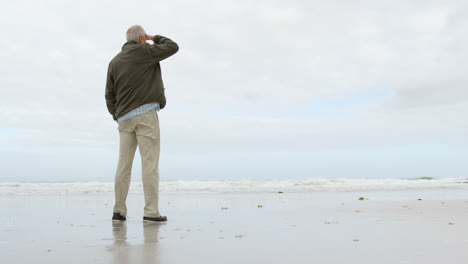 rear view of old caucasian senior man standing at beach 4k