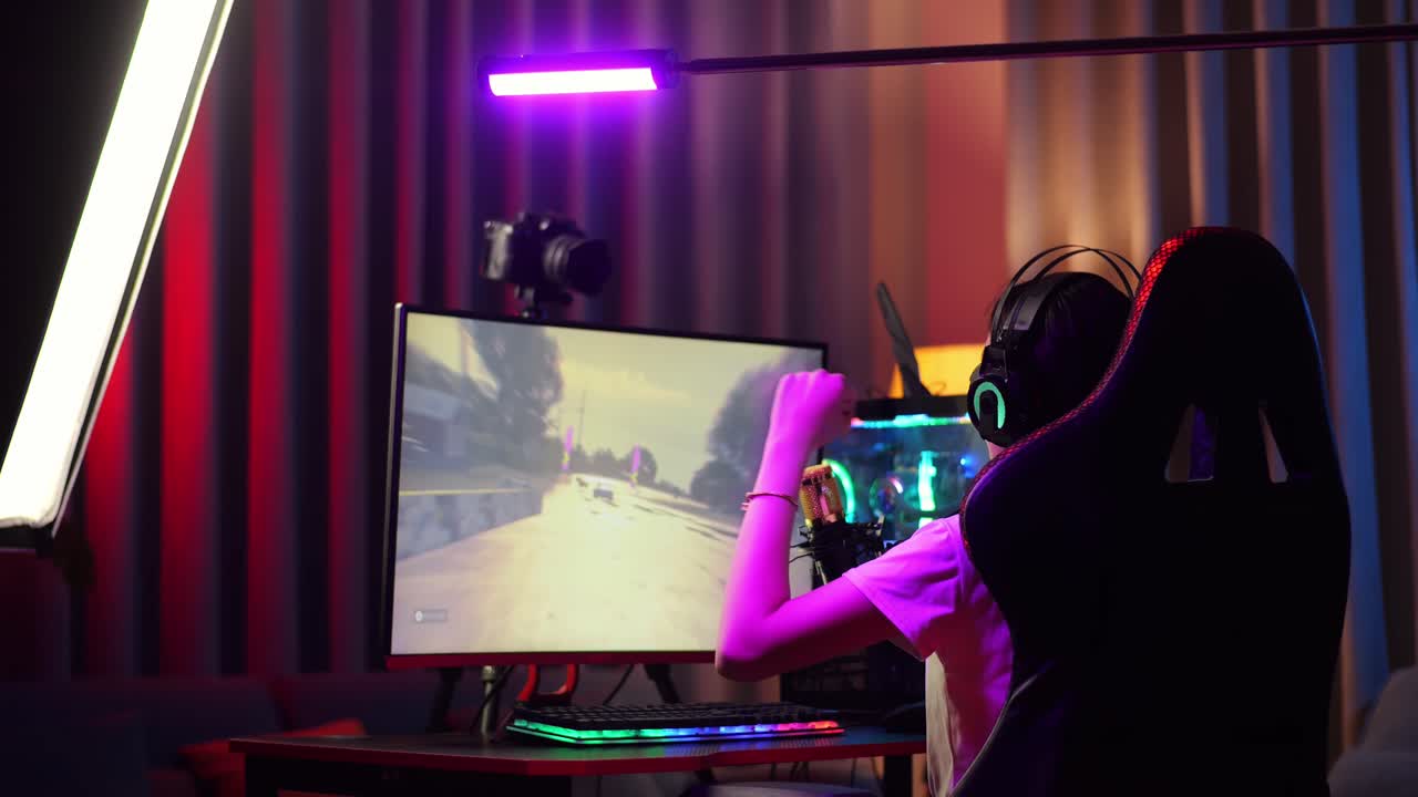 vista trasera de la chica asiática streamer gritando gol celebrando el juego de carreras de coches ganador a través de la red en la computadora personal. videojuego de transmisión en vivo, escritorio iluminado por luz de tira de led rgb