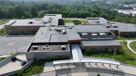 closed american high school campus with one black car on parking area. sunny summer day during vacation. aerial backwards wide shot. massachusetts, usa