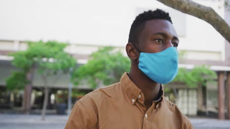 African-american-businessman-wearing-face-mask-sitting-in-park