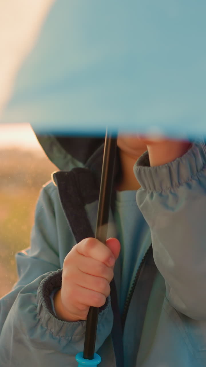 아이는 비가 오는 공원에서 우산을 돌립니다. 재미있는 사랑하는 작은 소년은 봄 폭풍 아래 무지개 우산으로 놀고 있습니다. 귀여운 아이는 해가 지는 에서 놀습니다.