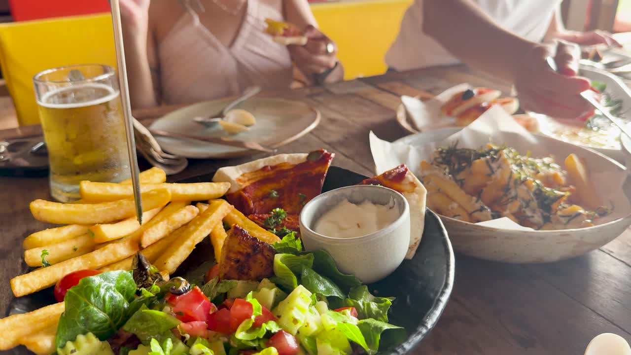 Casual dining scene with beer, fries, salad, and pizza at a beach club in Phuket, Thailand. Warm lighting and relaxed atmosphere