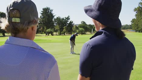 Kaukasischer-älterer-Mann,-Der-An-Einem-Strahlend-Sonnigen-Tag-Golf-Auf-Dem-Golfplatz-übt,-Während-ältere-Leute-Zuschauen