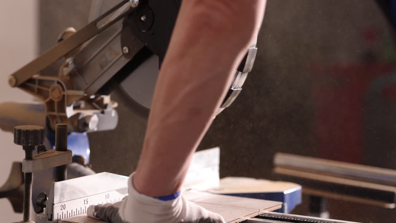 Close-up of a person using a miter saw to cut wood or laminate, generating sawdust
