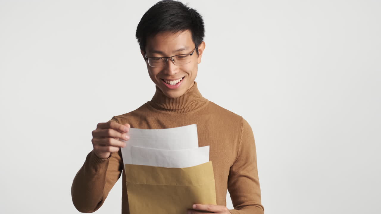 행복한 아시아인 남자가 봉투를 열고 내용을 읽습니다.
