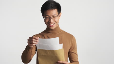 un hombre asiático feliz abriendo un sobre y leyendo el contenido.