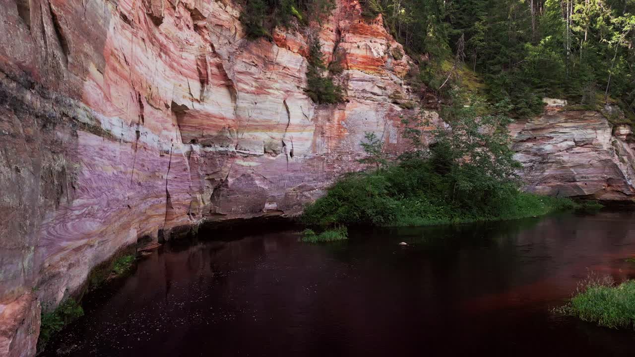 This close aerial perspective highlights the unique texture and scale of Taevaskoja sandstone cliffs with a calm river and dense forest creating a captivating Estonian outdoor scene