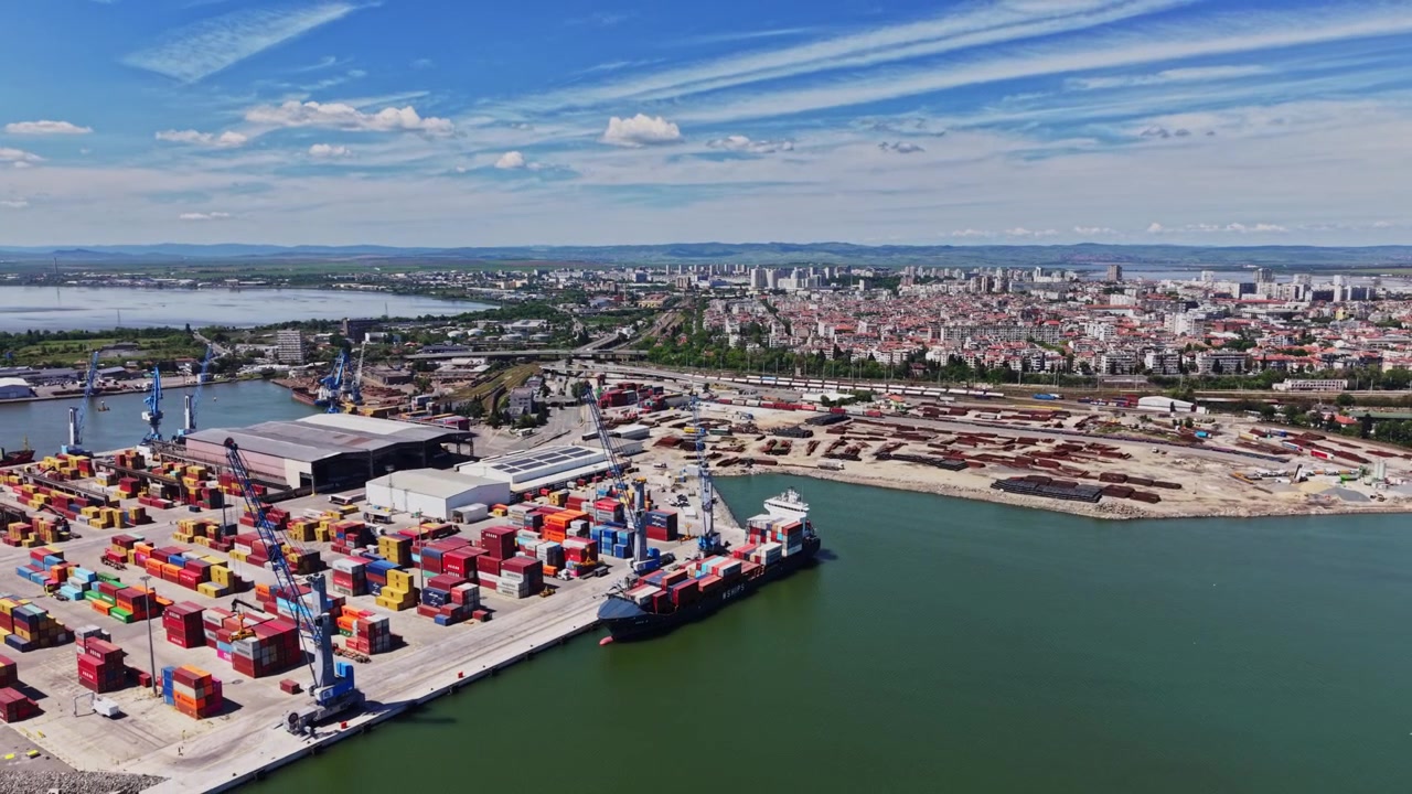 Vista di un'area portuale trafficata con container marittimi e lo skyline della città.