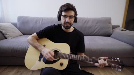 Portrait-of-a-man-with-a-guitar-playing-and-looking-at-the-camera-at-living-room