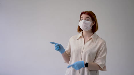mujer con máscara facial médica y guantes apuntando a un espacio en blanco vacío. espacio de copia y fondo blanco. vista frontal.