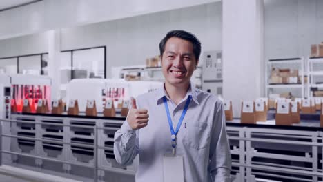 shot captures of an asian male professional worker standing with conveyor for packaging coffee beans in bags at coffee factory, his broad smile at the camera and thumbs up