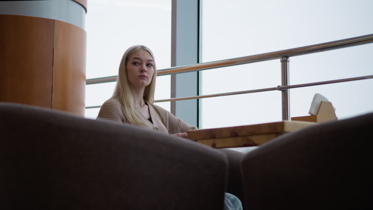 dama elegante sentada en una mesa de restaurante, mirando tenso mientras espera a alguien con la mano en la mesa de madera y el marco de vidrio transparente del edificio