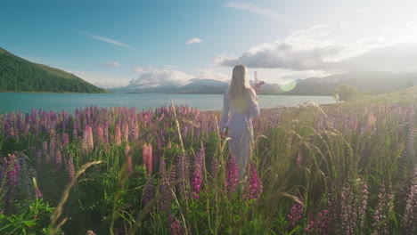 Blond-female-model-in-white-dress-walks-through-lupin-flower-field-at-bright-sunrise