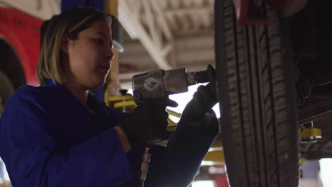 female mechanic changing tires of the car using a power drill at a car service station