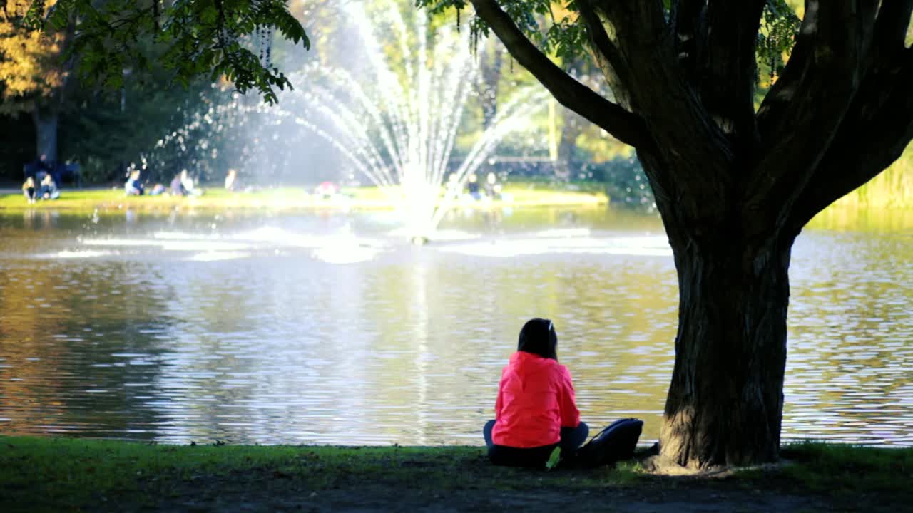 Woman in pink coat looking out over water with fountain in park