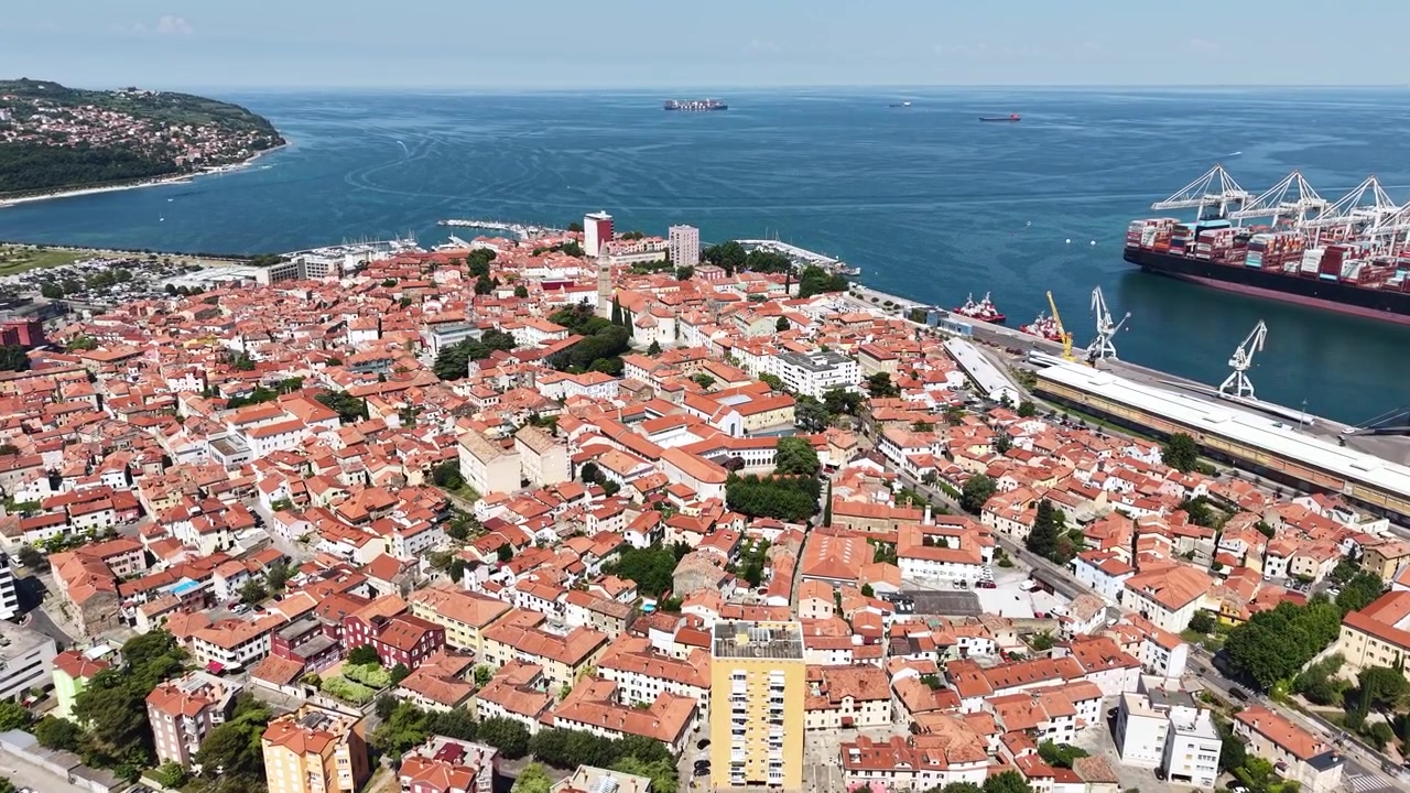 Ripresa aerea con drone di Capodistria, Slovenia, centro storico e porto cittadino con navi portacontainer in una calda giornata di sole.