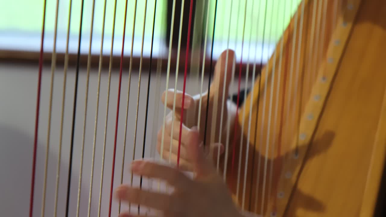 A close up of the hands of a female harpist playing harp solo during a performance.