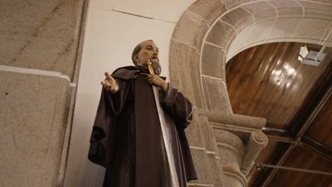 religious statue of a monk with a cross inside a church beside an arched stone structure