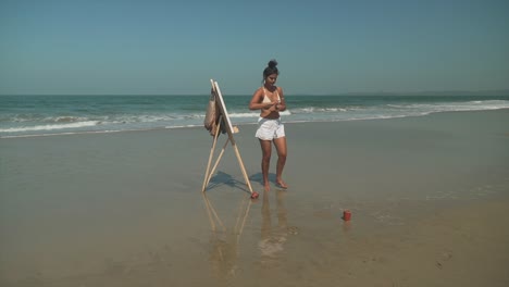 Joven-Artista-Creativa-Pintando-Un-Cuadro-Con-Pinturas-Acrílicas-En-Una-Hermosa-Playa-Soleada,-Artística,-Expresión,-Estudio