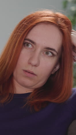 distressed woman tries to find interesting tv program to watch at home after work. redhead housewife leans head on hand holding remote control closeup