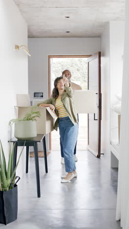 vertical video of happy diverse mature couple moving into home carrying boxes, slow motion