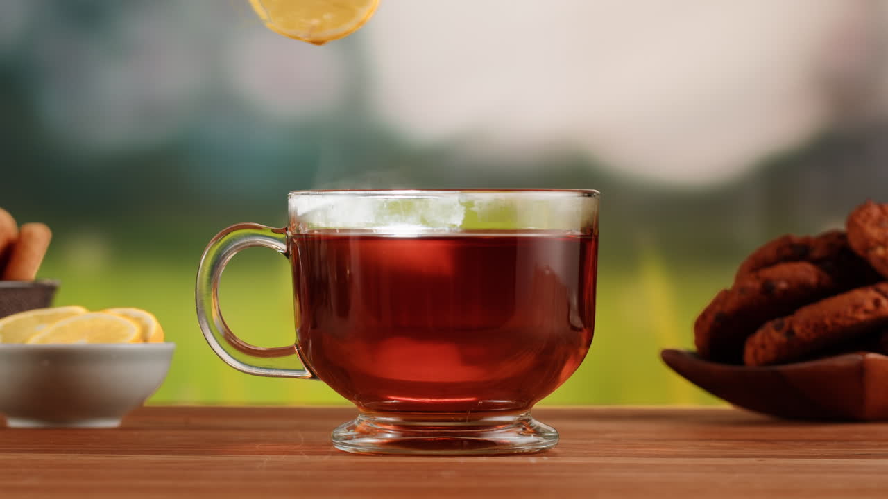 A steaming mug of tea with cookies and lemon slices