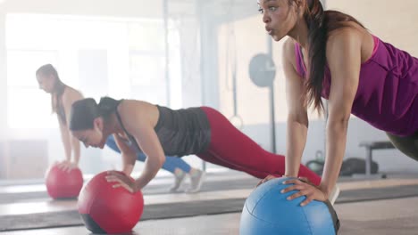 determined unaltered diverse women doing push ups on medicine balls at fitness class, slow motion