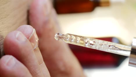 close-up of hand applying cuticle oil or serum with dropper for nail care