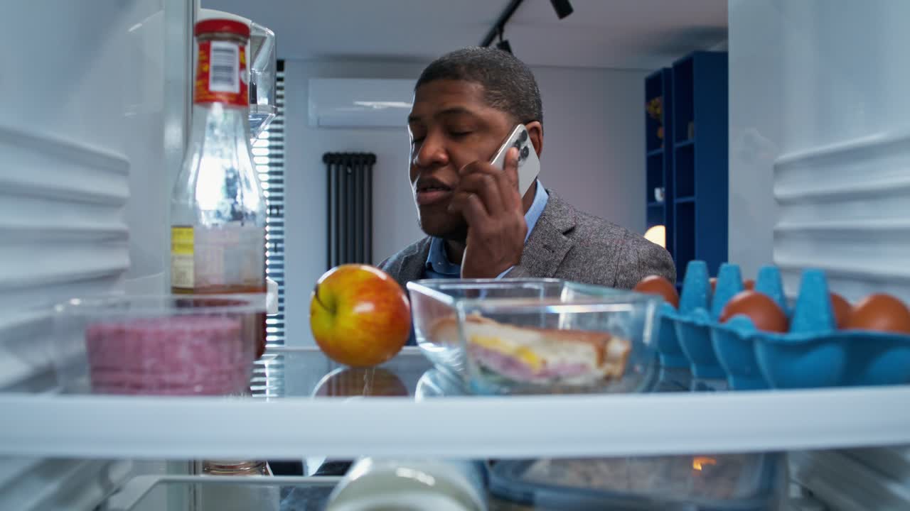 hombre comprobando el refrigerador mientras habla por teléfono