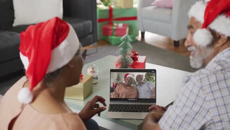 Happy-senior-african-american-couple-on-video-call-on-laptop-with-senior-friends-at-christmas-time