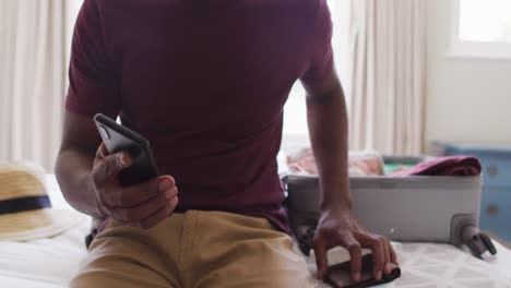 midsection of biracial man preparing for travel, showing smartphone with covid-19 passport on screen