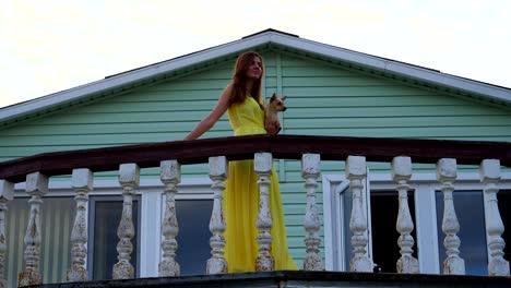 woman holds a small dog in her arms and goes to the balcony along the railing