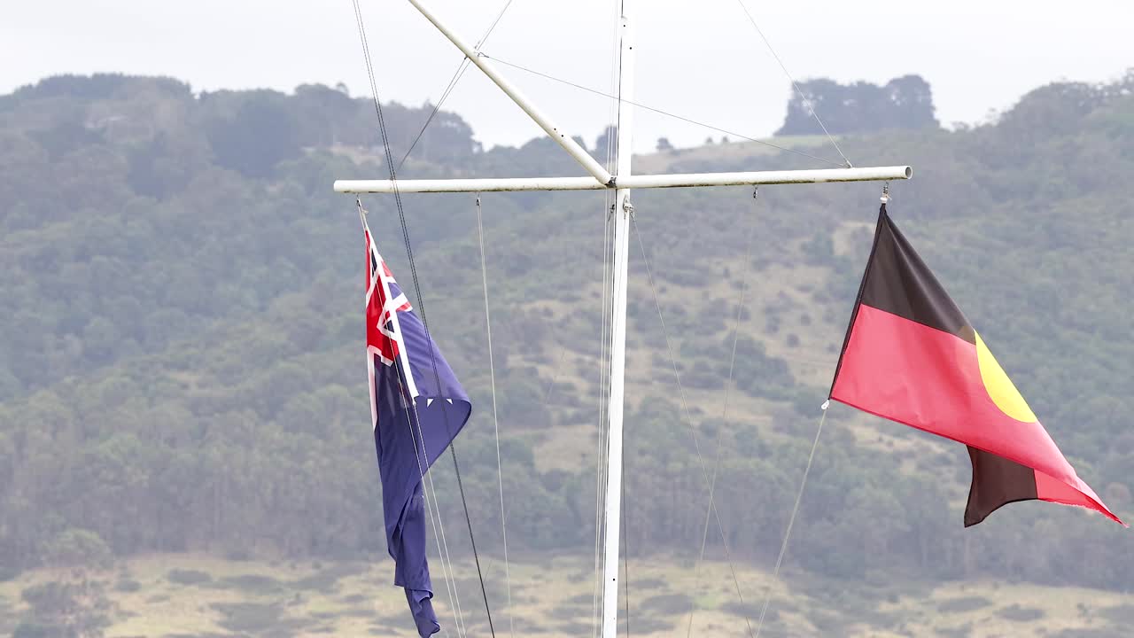 Australian and Aboriginal flags flutter in the wind against a scenic backdrop, captured in natural daylight with a steady camera