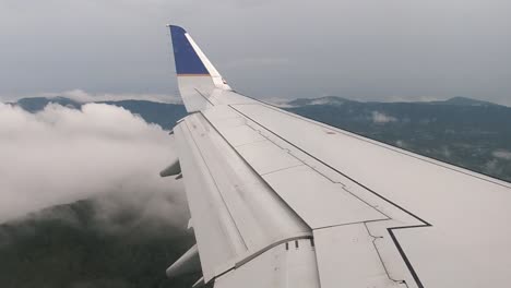 Blick-Entlang-Des-Flugzeugflügels,-Der-über-Wolken-Fliegt,-Mit-Blauen-Bergrücken-Im-Hintergrund