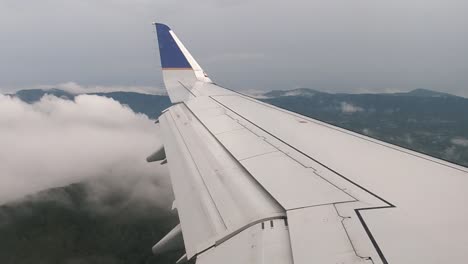 vista mirando a lo largo del ala del avión volando sobre nubes con montañas de cresta azul en el fondo