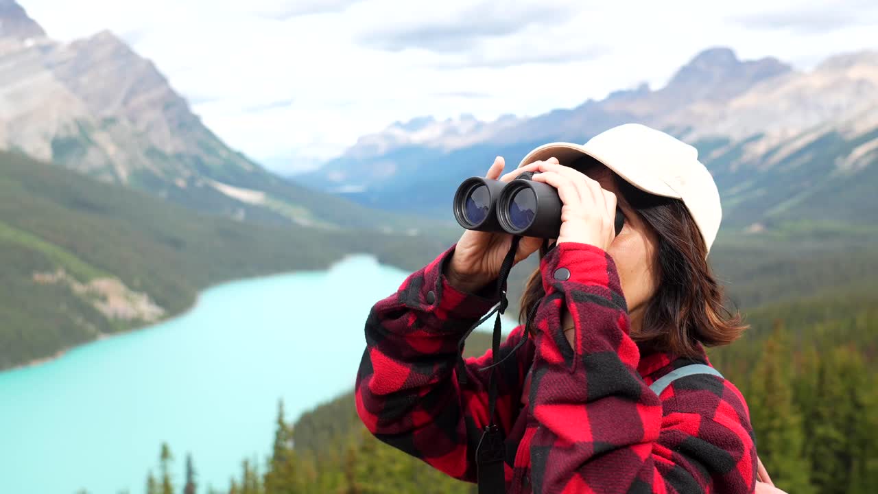 Woman using binoculars overlooking a lake in the mountains