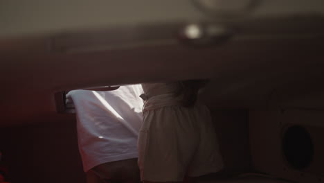 little children stand leaning out of motorboat hatch in salon on sea trip. curious brother and sister ride yacht together on summer vacation. family time