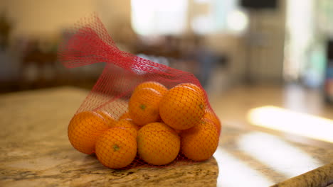 foto de trípode de un hombre que deja caer una bolsa de naranjas en un mostrador de cocina en un día cálido y soleado