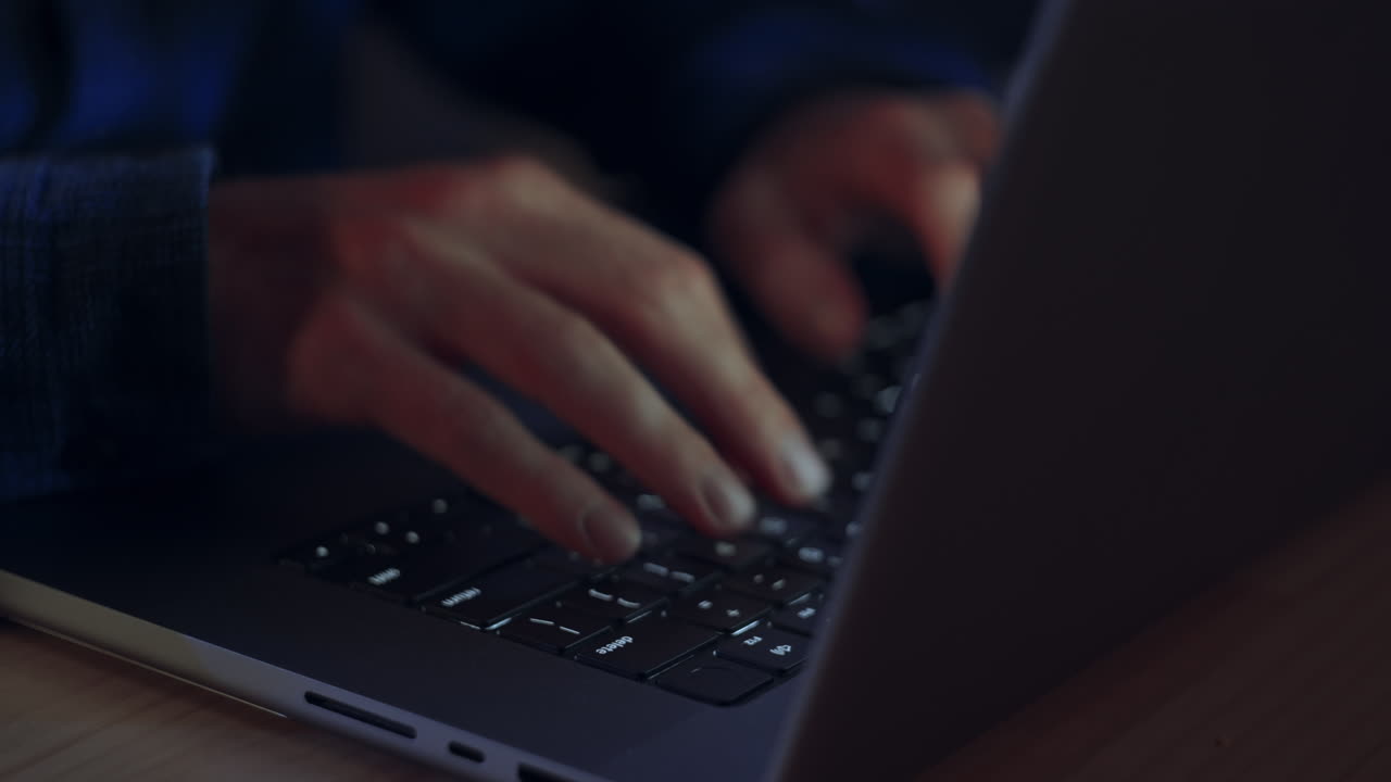 Close up of a man's hands as he types on a laptop during the evening - the screen being only what illuminates his hands