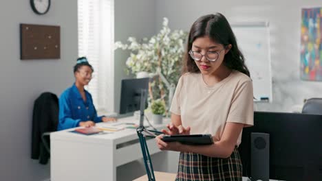 gerente del departamento de contabilidad, hermosa chica con gafas sostiene la tableta en la mano, comprueba el progreso del trabajo en la tableta, delega a su colega para que se encargue de crear informes, documentos