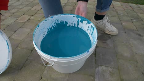 close up of a girls hand is opening a paint bucket wih blue paint