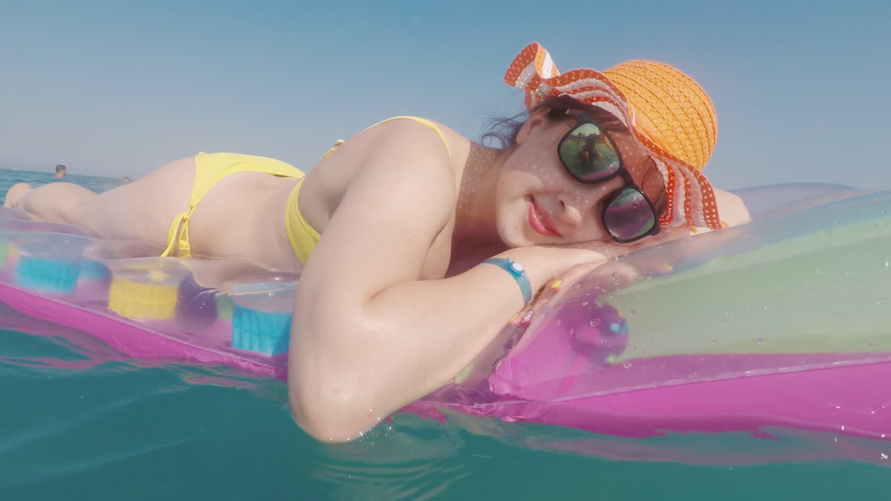 mujer atractiva con un sombrero naranja flota en el mar sobre un colchón inflable