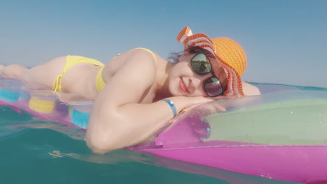 mujer atractiva con un sombrero naranja flota en el mar sobre un colchón inflable