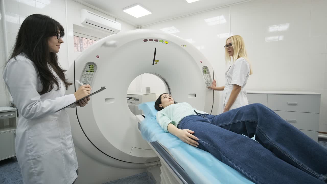 la paciente está siendo sometida a una tomografía computarizada o resonancia magnética bajo la supervisión de dos radiólogos calificados en una clínica médica moderna. la paciente está acostada en una mesa de tomografías computarizadas o mri, moviéndose fuera de la máquina