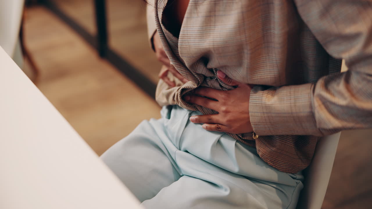 Woman holding her stomach in pain while sitting at a table in an office