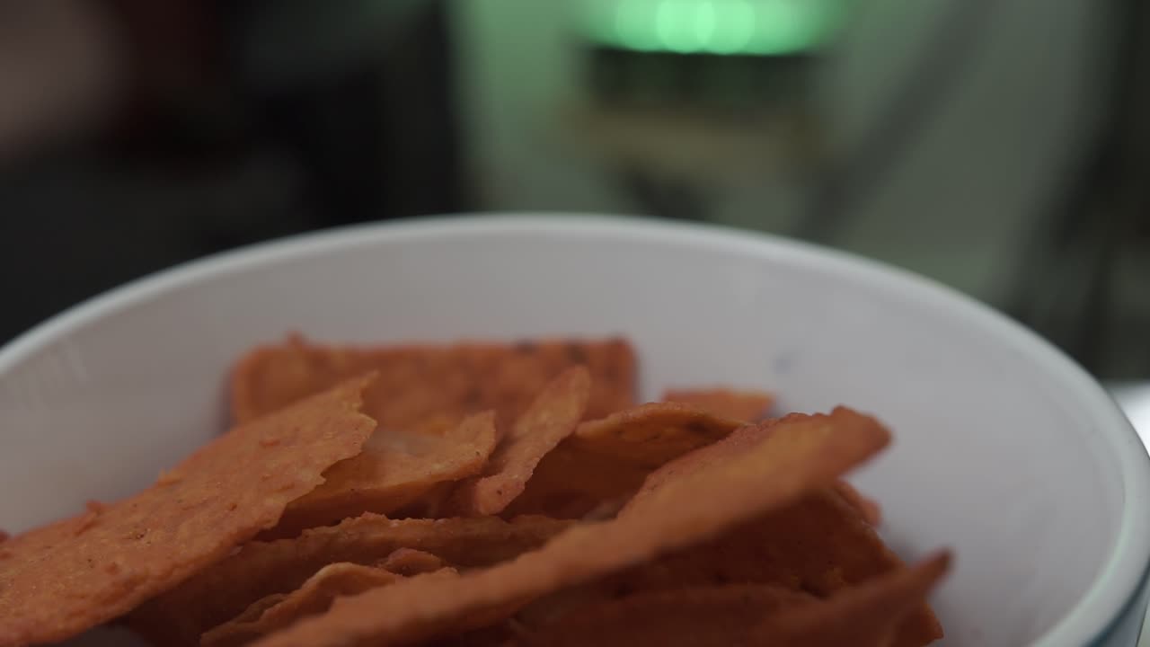Close-up shot of nachos in white bowl with green light and blurred human silhouette